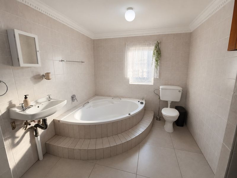 A functional bathroom featuring a corner bathtub, pedestal sink, and toilet with neutral wall and floor tiling.