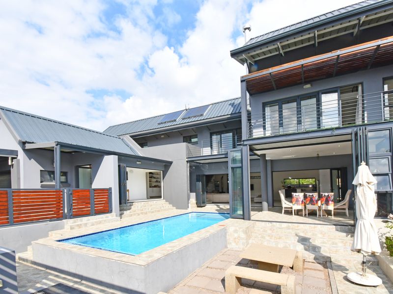 Rear view of a modern multi-story home featuring a swimming pool, stone patio, and seamless indoor-outdoor flow through large folding glass doors.