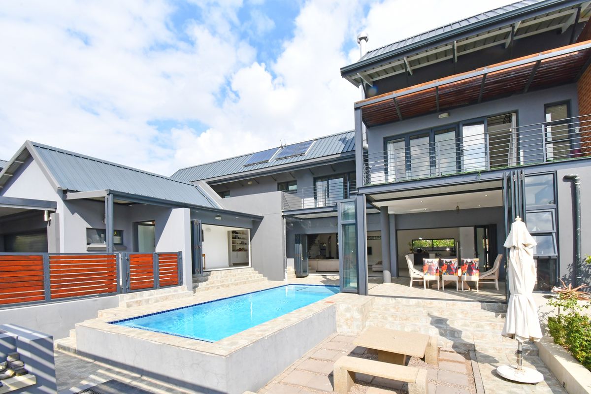 Rear view of a modern multi-story home featuring a swimming pool, stone patio, and seamless indoor-outdoor flow through large folding glass doors.