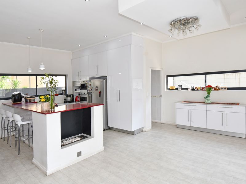 Modern open-plan kitchen featuring high-gloss white cabinetry, a red-topped island with integrated fireplace, and sleek horizontal windows providing natural light.