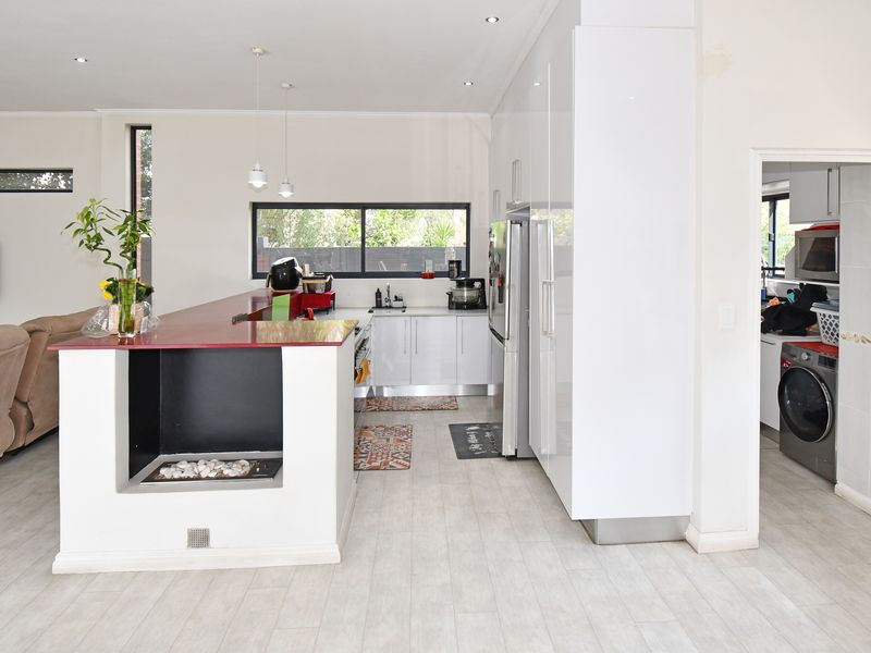 Modern open-plan living area featuring a sleek kitchen with high-gloss cabinetry, a built-in fireplace, and direct access to a separate laundry room.