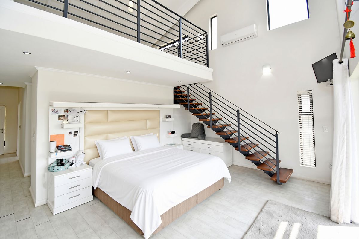 Spacious loft-style bedroom featuring a mezzanine level, modern metal staircase, tiled flooring, and built-in headboard with integrated lighting.