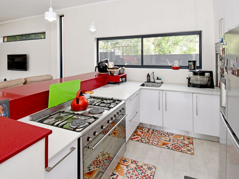 Modern kitchen featuring white cabinetry, striking red stone benchtops, a gas cooktop with freestanding oven, and a functional layout overlooking the living area.