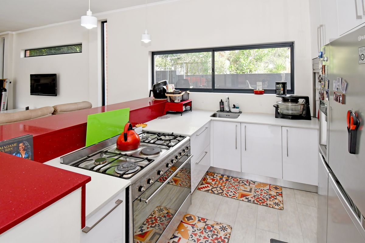 Modern kitchen featuring white cabinetry, striking red stone benchtops, a gas cooktop with freestanding oven, and a functional layout overlooking the living area.