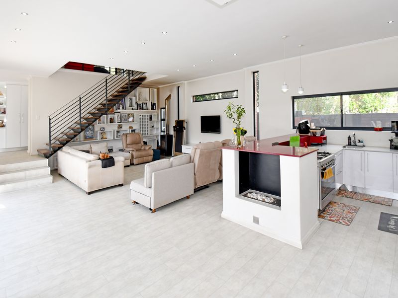 Spacious open-plan living area featuring a modern kitchen with island, integrated gas fireplace, and a striking metal staircase leading to the upper level.