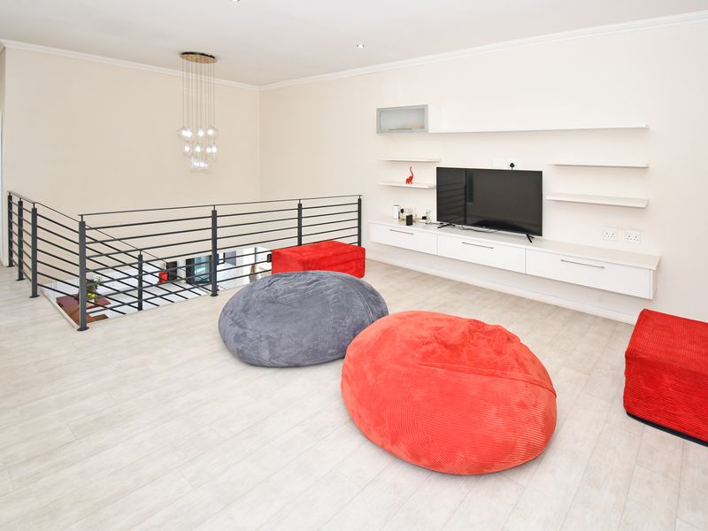 Spacious living area featuring a modern floating media console, wall-mounted shelving, and a sleek metal balustrade overlooking the lower level.