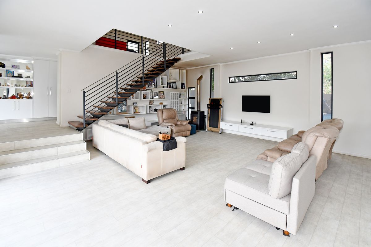 Spacious open-plan living area featuring a modern staircase, built-in shelving, a wood-burning fireplace, and light-toned tiled flooring.