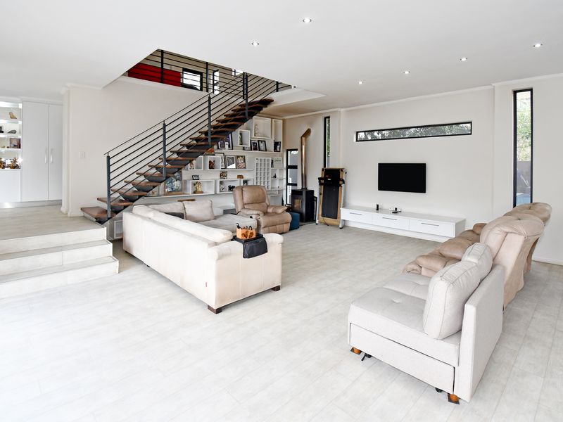Spacious open-plan living area featuring a modern staircase, built-in shelving, a wood-burning fireplace, and light-toned tiled flooring.