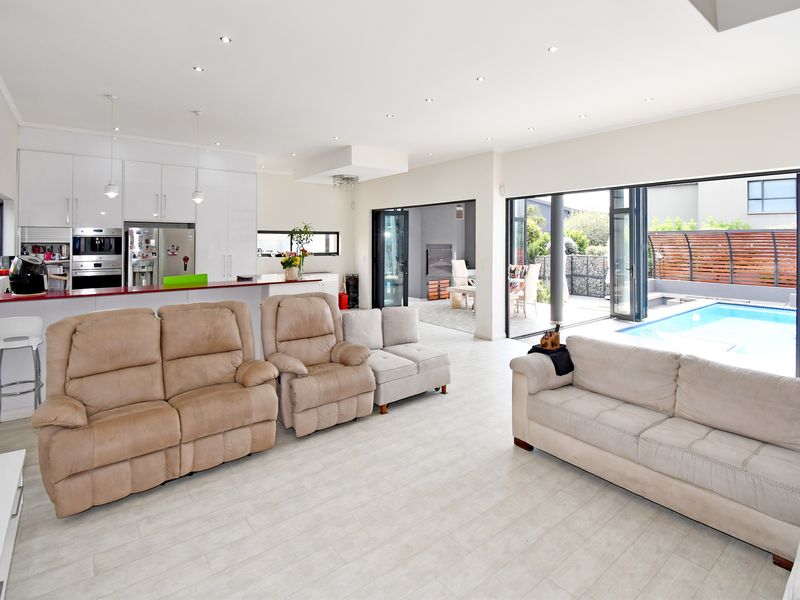 Spacious open-plan living area featuring a modern kitchen with integrated appliances, flowing seamlessly through bi-fold doors to an outdoor patio and pool area.