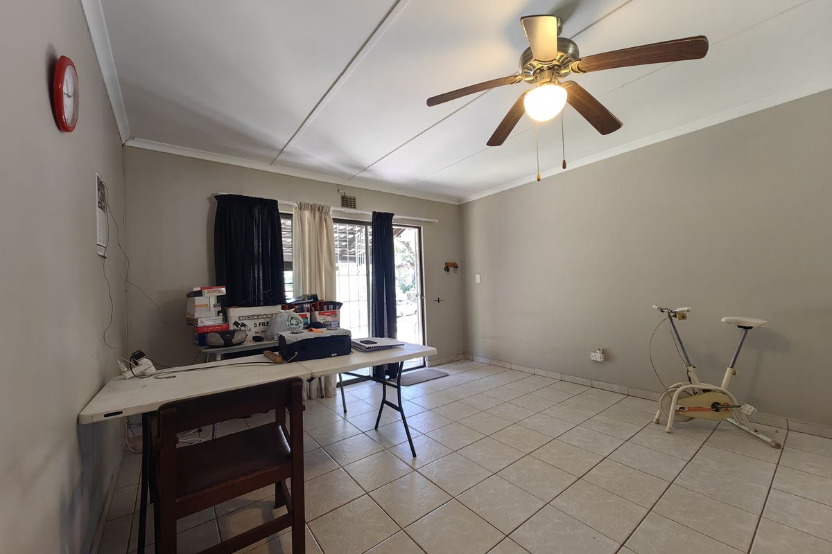 A spacious living area featuring neutral wall tones, tiled flooring, and a ceiling fan, with direct access to the outdoor area via sliding glass doors.