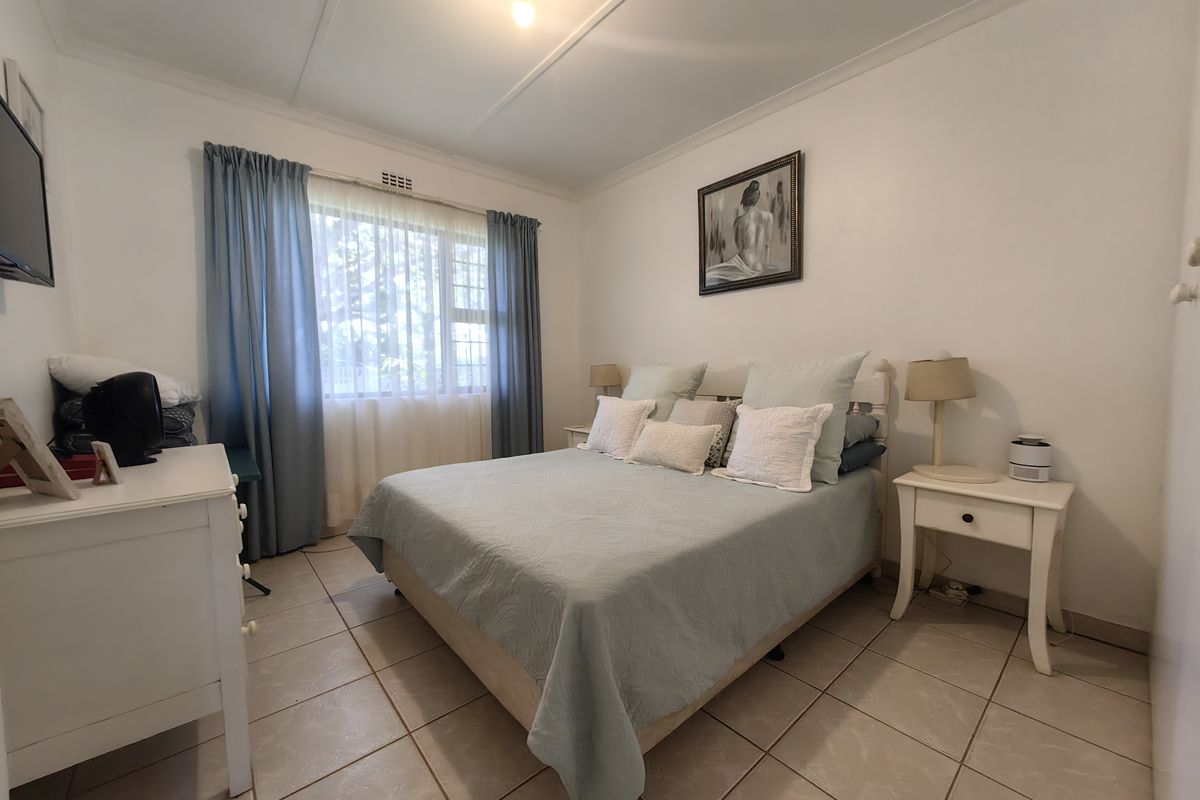 A functional bedroom featuring tiled flooring, a built-in cupboard, and a window fitted with security burglar bars.