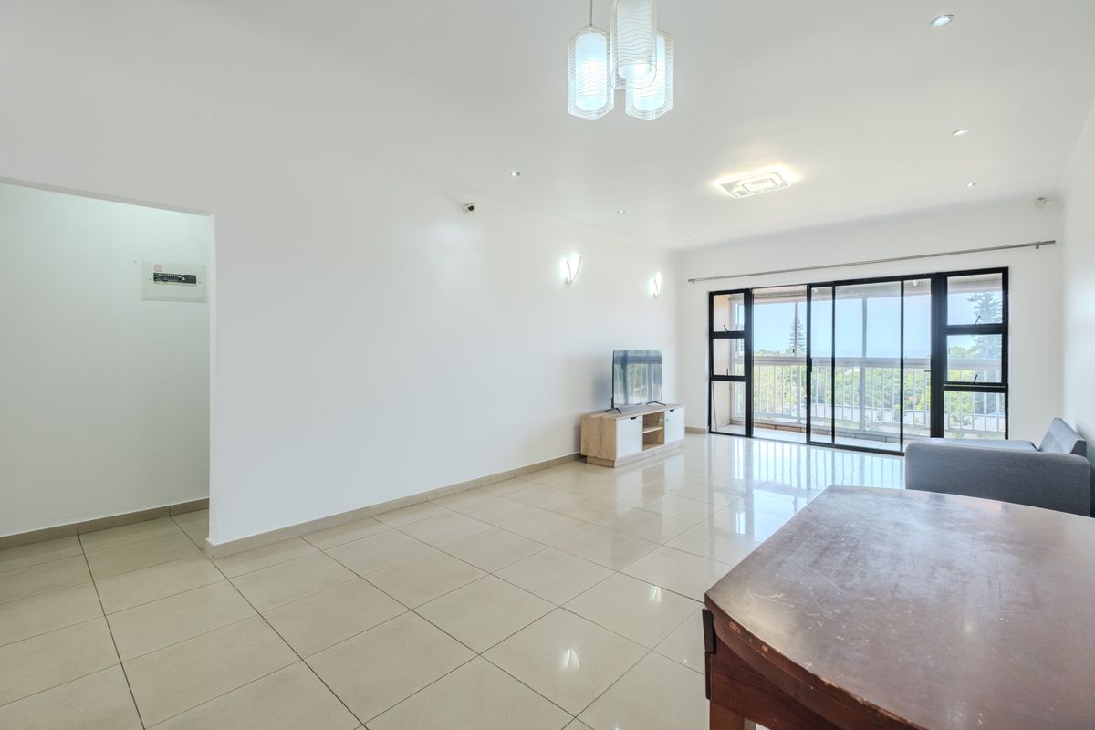 Spacious open-plan living area featuring polished porcelain floor tiles, modern lighting fixtures, and large sliding glass doors leading to a balcony.