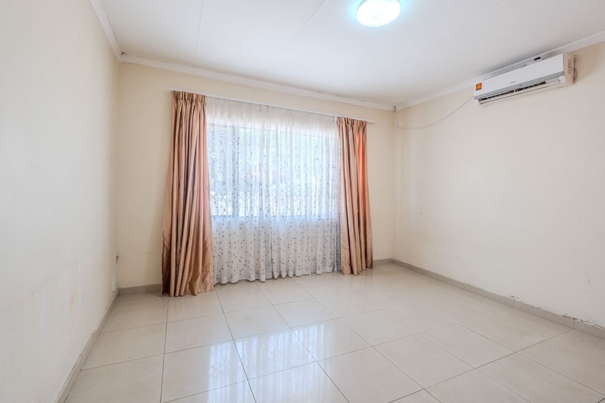 A bright, empty bedroom featuring tiled flooring, a wall-mounted air conditioning unit, and neutral wall finishes.