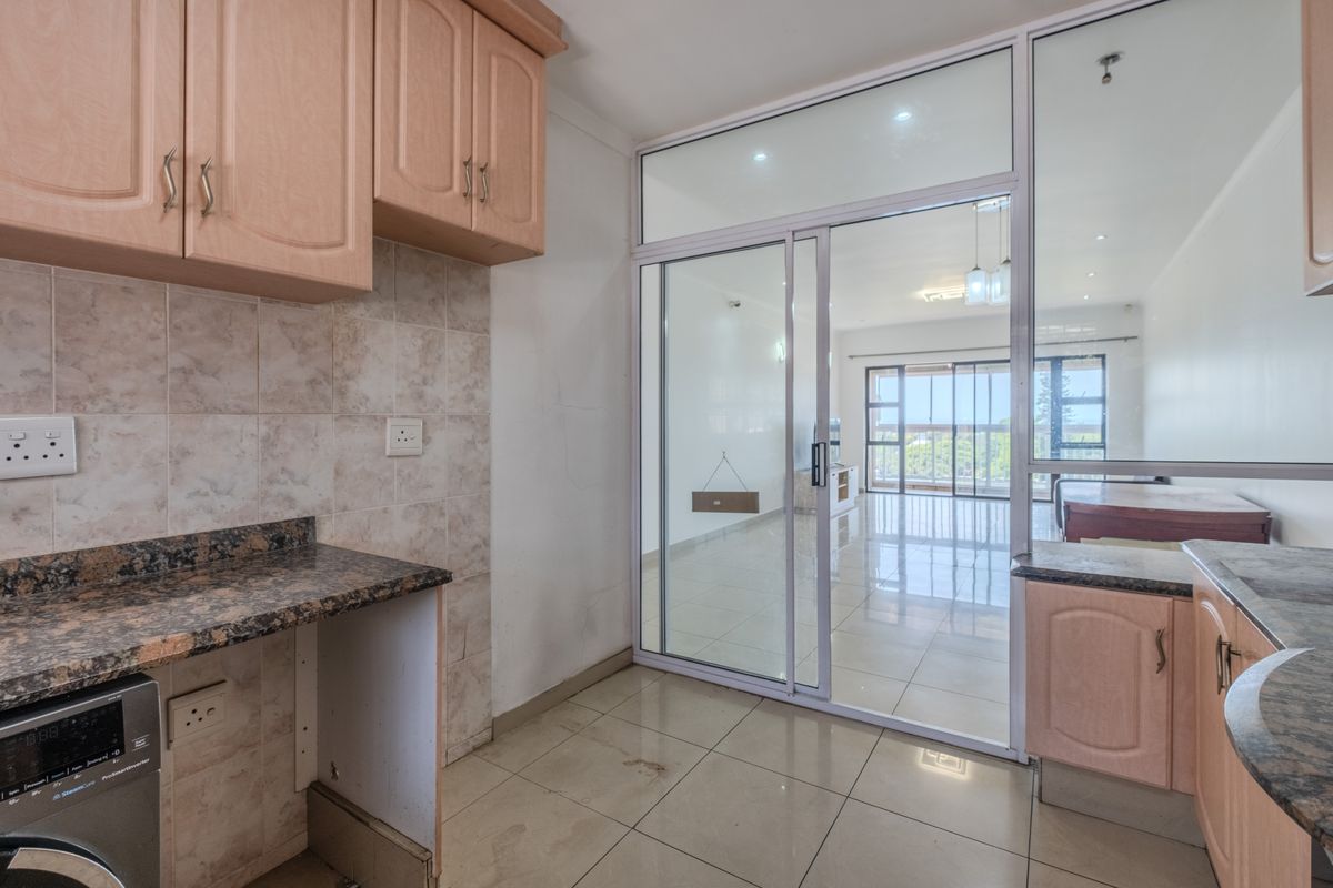 Compact kitchen featuring laminate cabinetry, granite countertops, and a sliding glass partition opening into the living area with tiled flooring throughout.