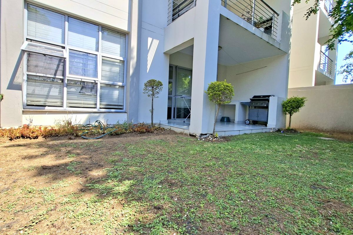 Rear view of the apartment featuring a tiled patio with a built-in braai, overlooking a private garden area with established boundary walls.