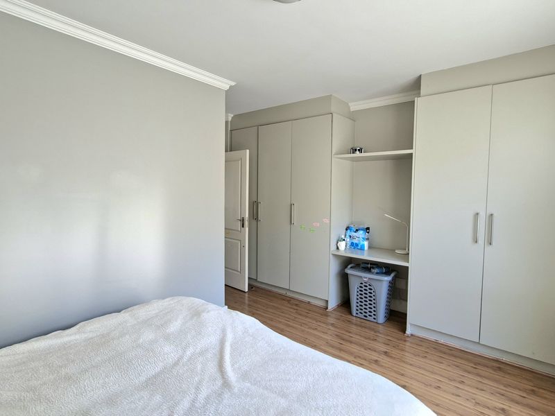 A well-maintained bedroom featuring neutral walls, laminate flooring, crown molding, and extensive built-in cupboard storage with an integrated desk area.