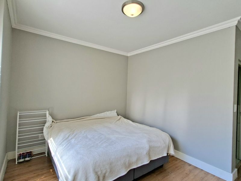 A well-maintained bedroom featuring laminate flooring, crown molding, and neutral wall tones, offering a clean and functional living space.