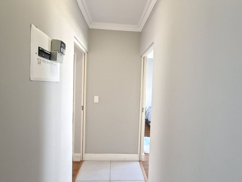 A clean and well-maintained hallway featuring tiled flooring, coving, and a wall-mounted electrical distribution board.