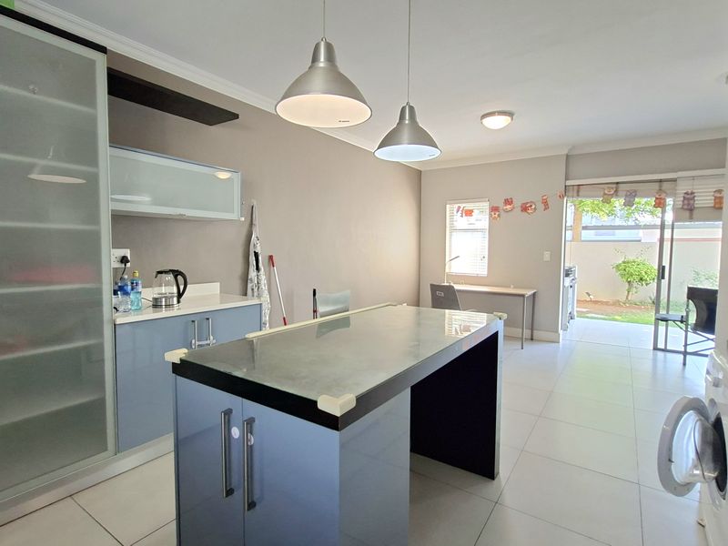 Open-plan kitchen and living area featuring modern cabinetry, a central island, tiled floors, and direct access to an outdoor patio through sliding glass doors.