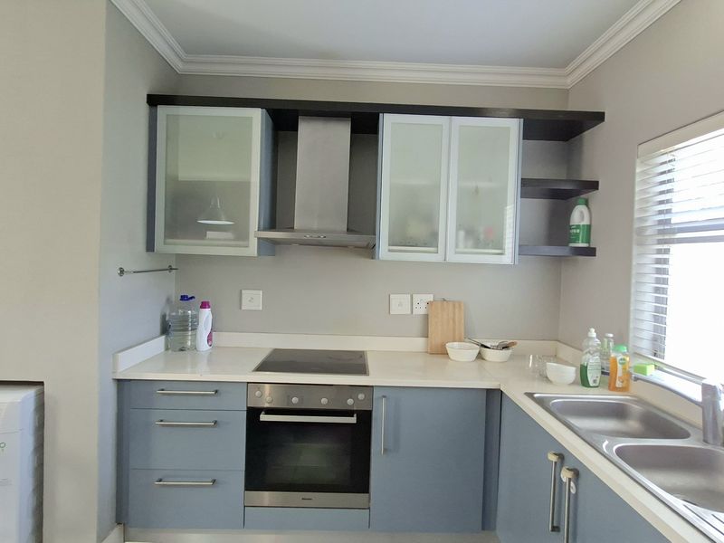 Modern kitchen featuring blue cabinetry, stone countertops, integrated oven and hob, stainless steel extractor fan, and a double bowl sink with natural light.