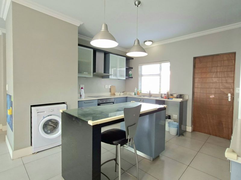 A functional kitchen featuring built-in cabinetry, integrated appliances, a central breakfast island, and tiled flooring, with an adjacent laundry connection point.