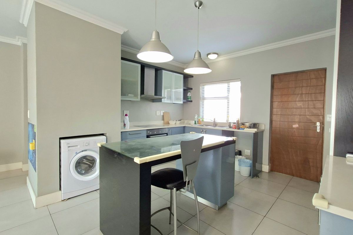 A functional kitchen featuring built-in cabinetry, integrated appliances, a central breakfast island, and tiled flooring, with an adjacent laundry connection point.