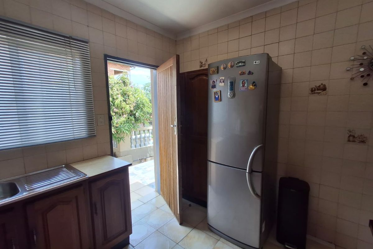 A functional kitchen area featuring tiled walls, built-in cabinetry, and a stainless steel sink, with direct access to an outdoor patio area.