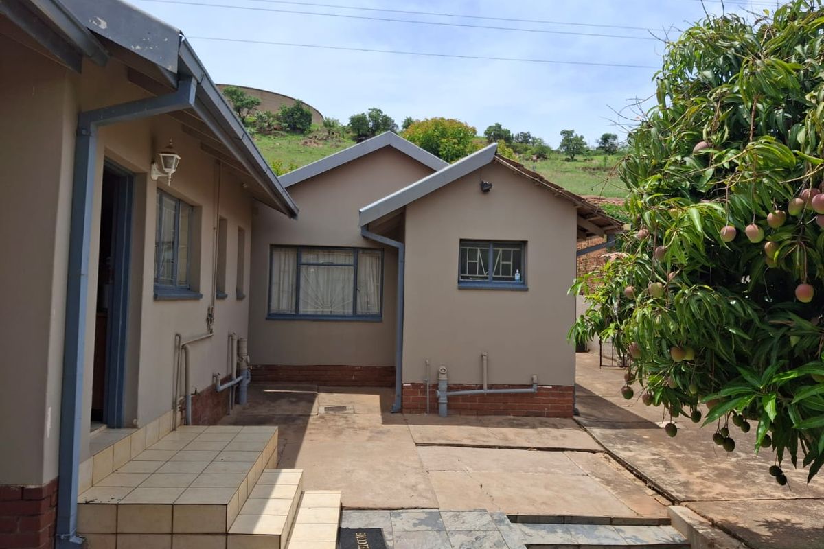 Rear exterior view of the house featuring a paved courtyard area, tiled entrance steps, and exposed brick foundation detailing.