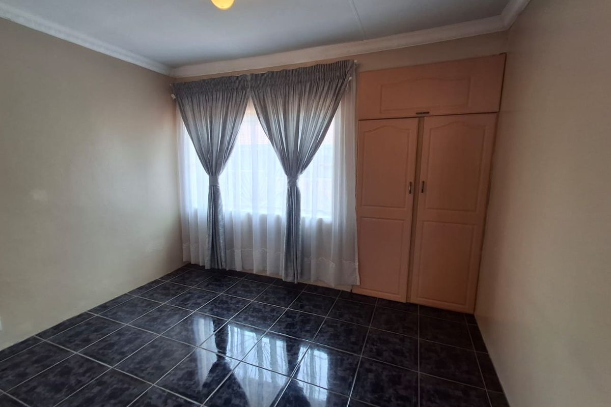 A clean, empty bedroom featuring dark tiled flooring, a built-in wardrobe, and neutral wall tones, offering a blank canvas for personalization.