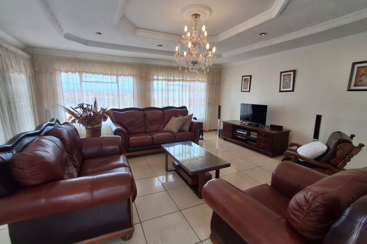 Spacious living room featuring tiled flooring, a decorative recessed ceiling with a crystal chandelier, and large windows allowing for ample natural light.