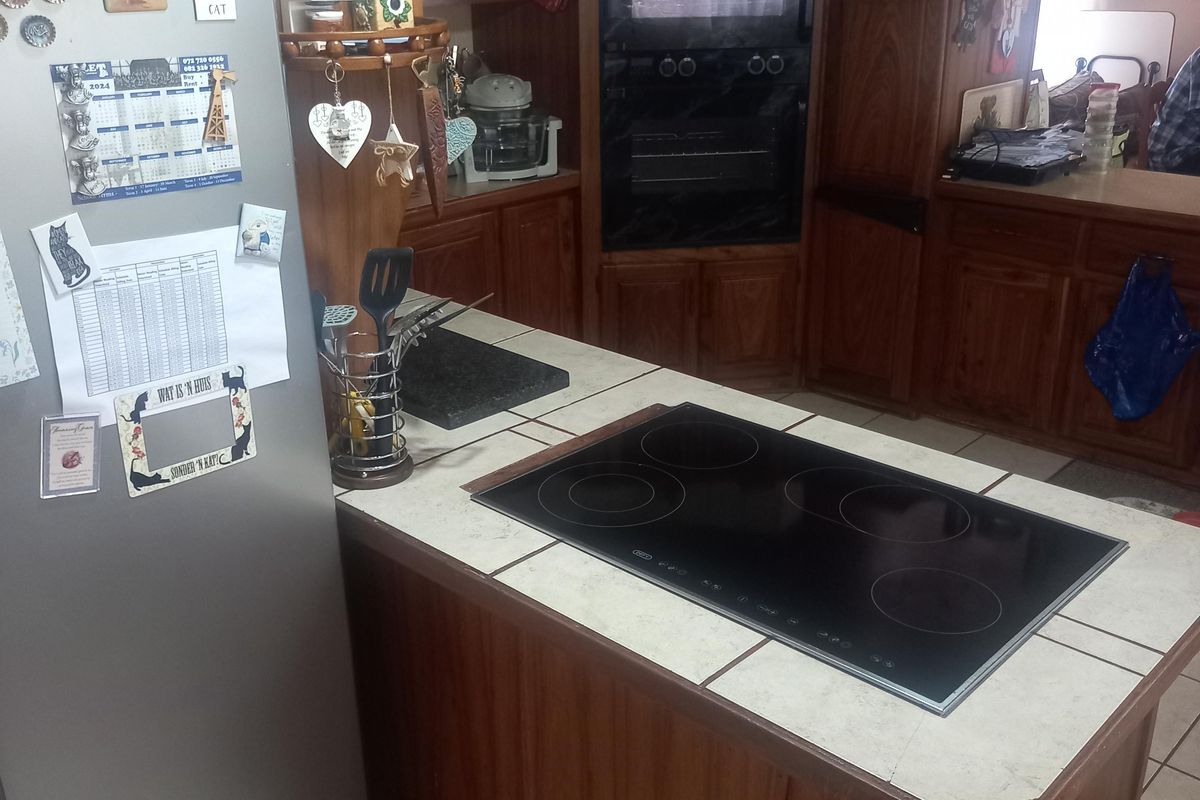 A functional kitchen featuring traditional wooden cabinetry, a tiled island with an integrated electric hob, and a built-in oven.