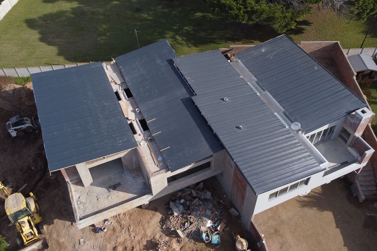 Aerial view of a duet property under construction, featuring a newly installed corrugated metal roof and ongoing exterior masonry work.
