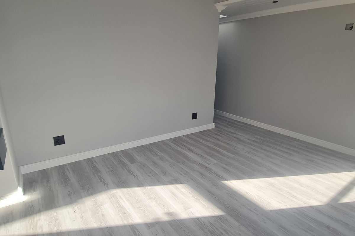 A bright, empty living area featuring modern light-toned laminate flooring, neutral grey walls, and a sleek wall-mounted cabinet.