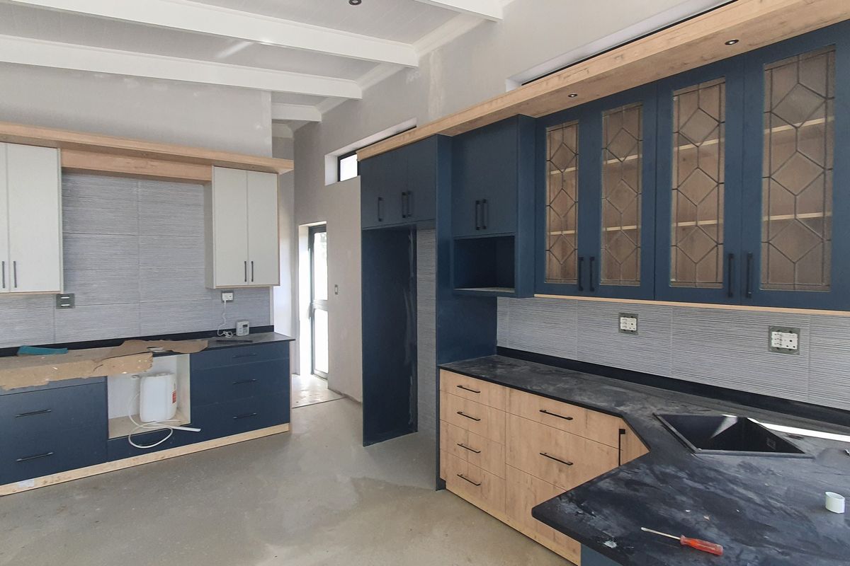 A modern kitchen under construction featuring two-tone cabinetry, stone countertops, and exposed ceiling beams, awaiting final finishes and appliance installation.