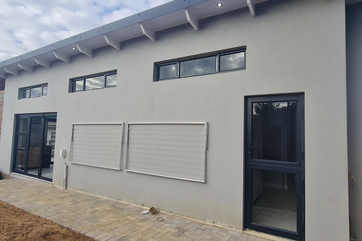 Rear exterior view of the duet property featuring a paved patio, modern aluminium doors and windows, and exposed rafter roof detailing.