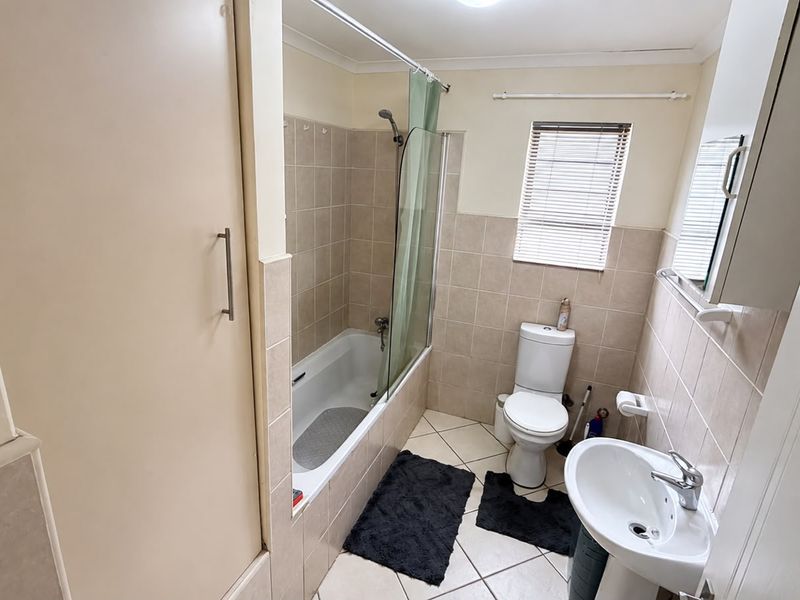 A functional bathroom featuring a bathtub with a shower screen, a pedestal basin, and a toilet, finished with neutral wall and floor tiles.