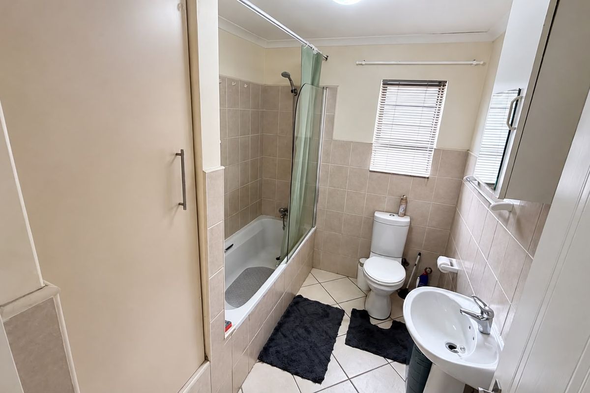 A functional bathroom featuring a bathtub with a shower screen, a pedestal basin, and a toilet, finished with neutral wall and floor tiles.