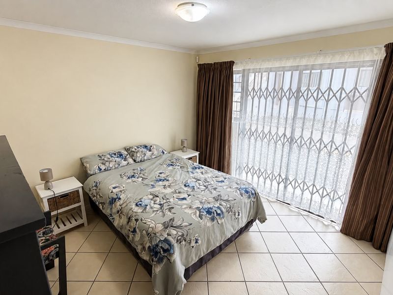 A bedroom featuring tiled flooring, built-in cupboards, and a sliding door with a security gate providing access to the exterior.