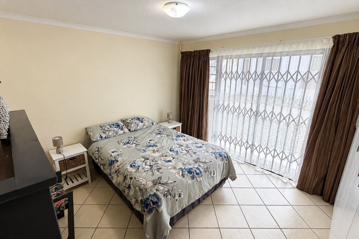A bedroom featuring tiled flooring, built-in cupboards, and a sliding door with a security gate providing access to the exterior.