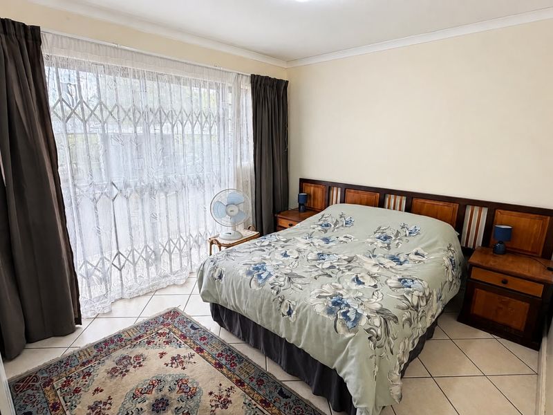 A bedroom featuring tiled flooring, a built-in wooden headboard, and a sliding door with a security gate leading to the exterior.