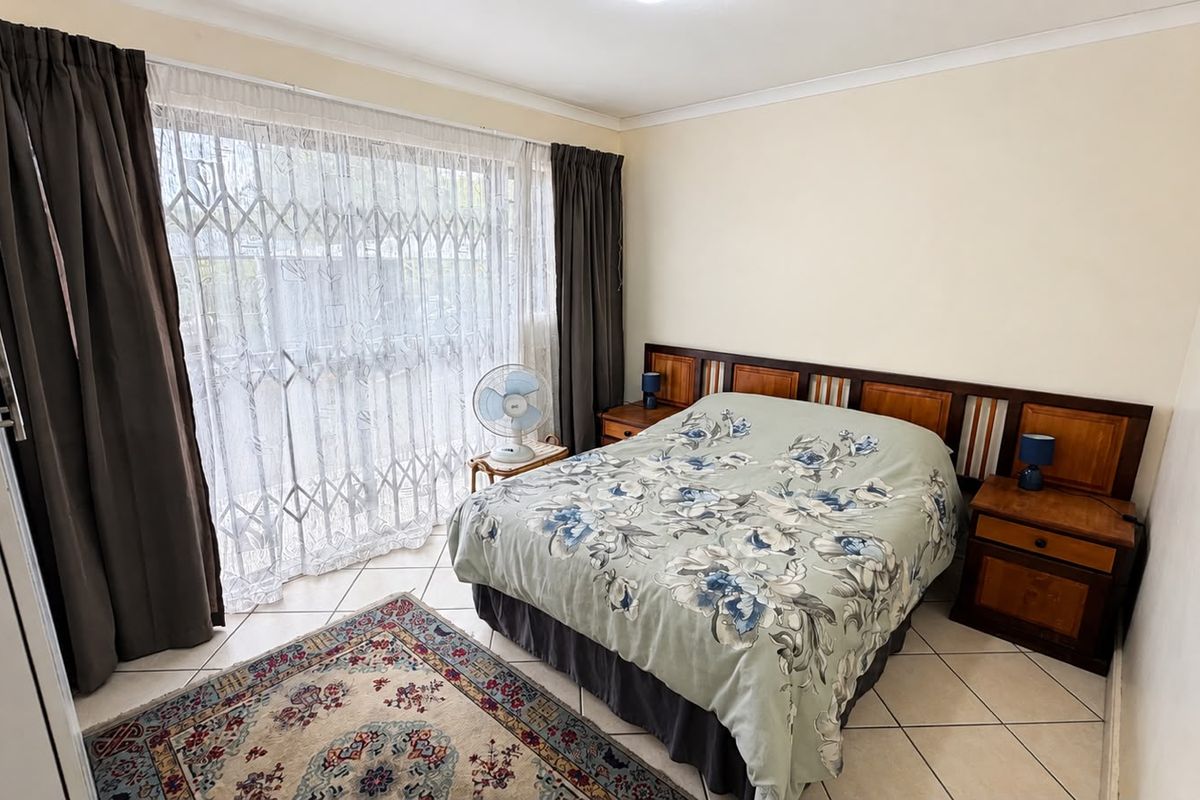 A bedroom featuring tiled flooring, a built-in wooden headboard, and a sliding door with a security gate leading to the exterior.