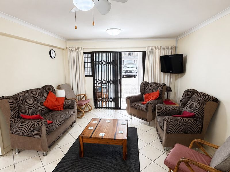 A comfortable living room featuring tiled flooring, a ceiling fan, and direct access to an outdoor area through a secure sliding gate.