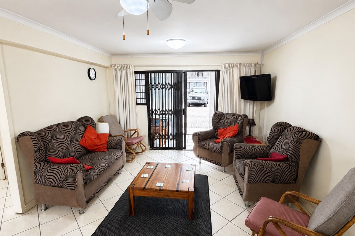 A comfortable living room featuring tiled flooring, a ceiling fan, and direct access to an outdoor area through a secure sliding gate.