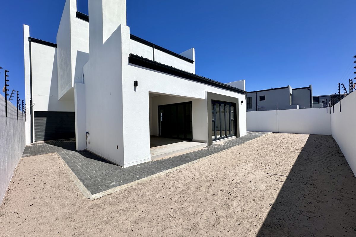 Modern rear exterior view of the property featuring a covered patio, paved walkway, and an expansive, undeveloped garden space.