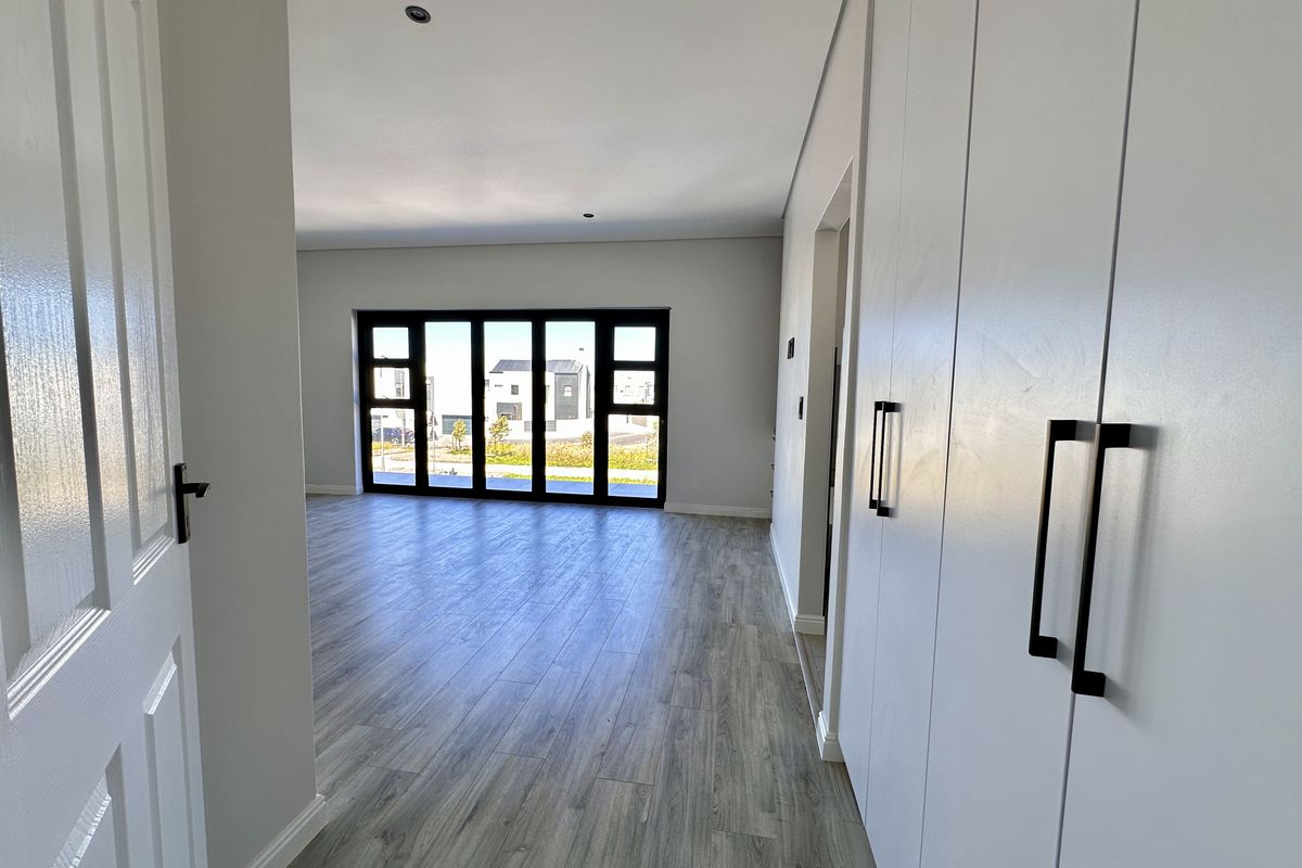 A bright, modern living area featuring wood-look flooring, built-in cabinetry, and large black-framed glass doors leading to the exterior.