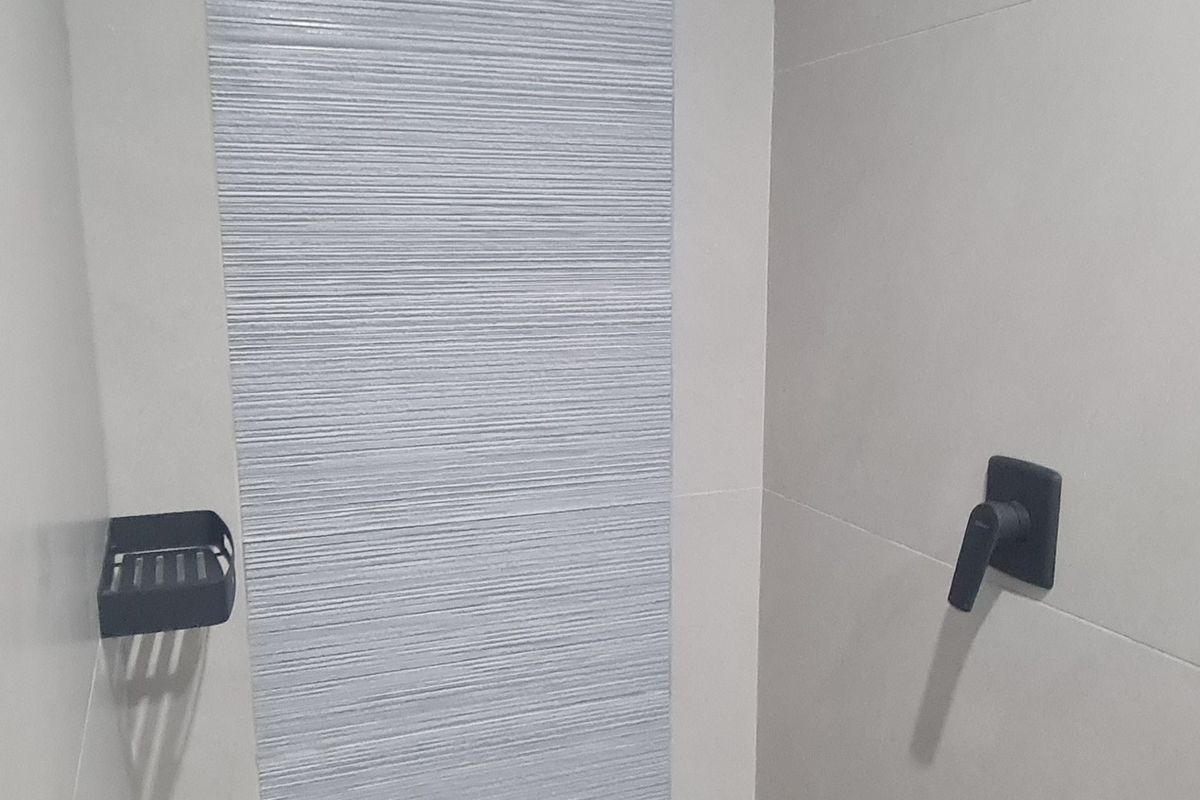 Modern walk-in shower featuring contemporary grey tiling, a sleek black rain shower head, and a linear floor drain.