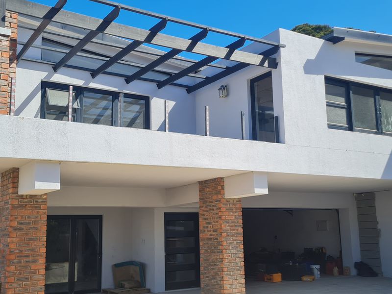 Rear view of the duet property featuring a spacious balcony with a pergola, brick pillar accents, and ground-level garage access.