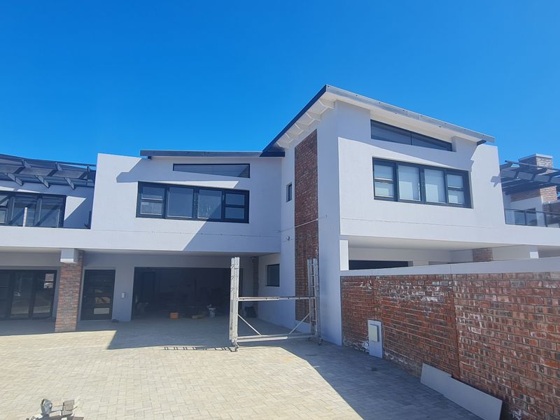 Front elevation of a modern duet property featuring a combination of brick and plaster finishes, paved driveway, and upper-level balconies under construction.