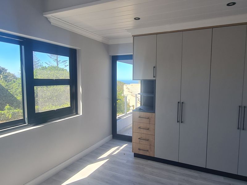 A bright, modern bedroom featuring extensive built-in cabinetry, sleek laminate flooring, and large windows that provide natural light and views.