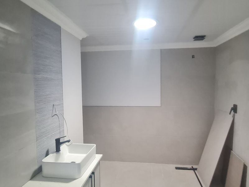 A bathroom under renovation featuring modern grey wall and floor tiles, a vessel sink vanity, and a skylight, currently in an unfinished state.